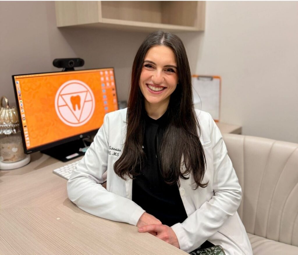 Dr. Jenna Schneider, board-certified orthodontist at First Impression Orthodontics in Alexandria, sitting at desk smiling